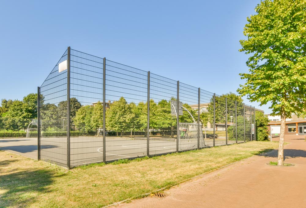 Professionell montierter Eisenzaun mit stabiler Einbetonierung und Pflasterarbeiten rund um einen Fußballplatz für mehr Sicherheit und klare Begrenzung.